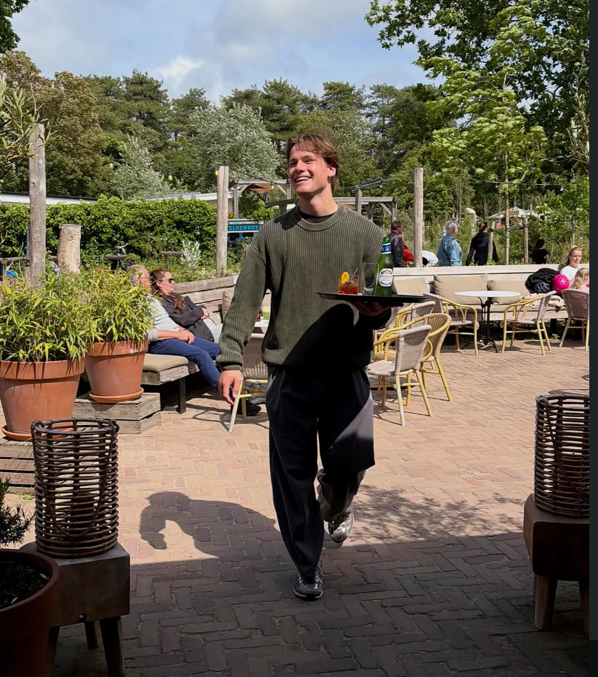 Bram carrying a serving tray at an outdoor terrace
